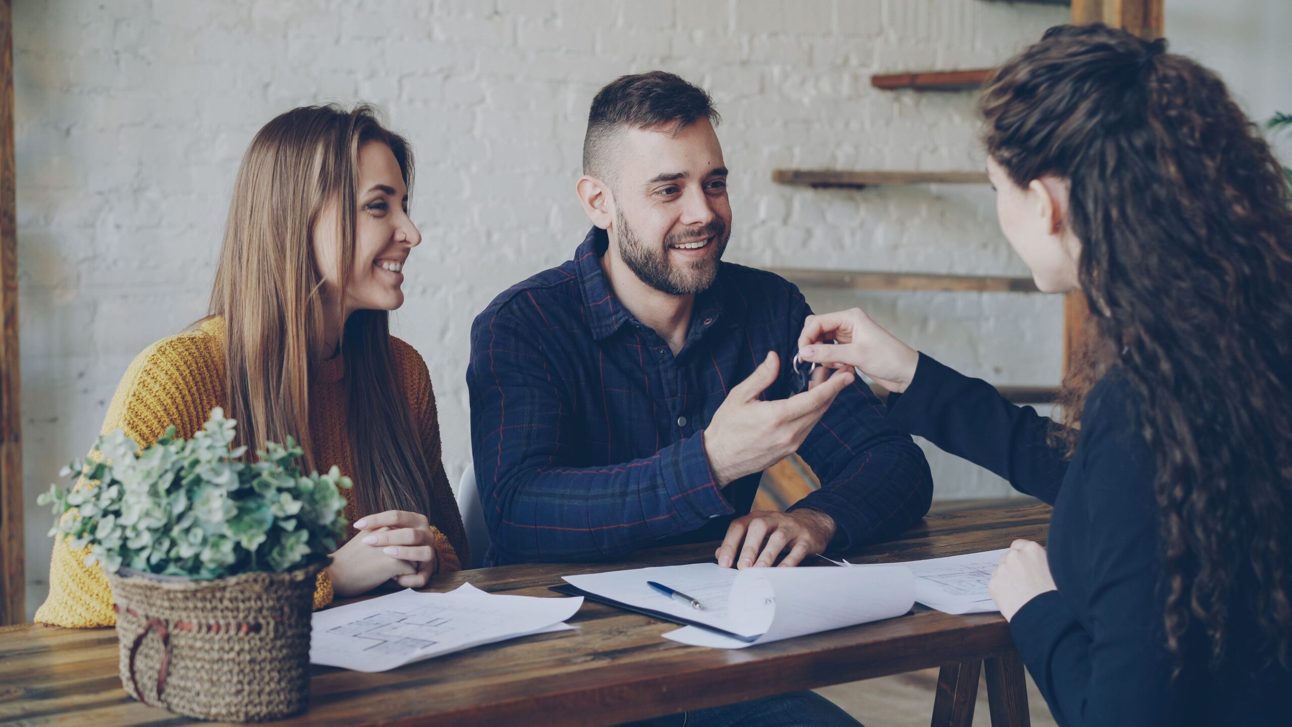 Smiling couple receiving house keys from a real estate agent at a wooden desk.
