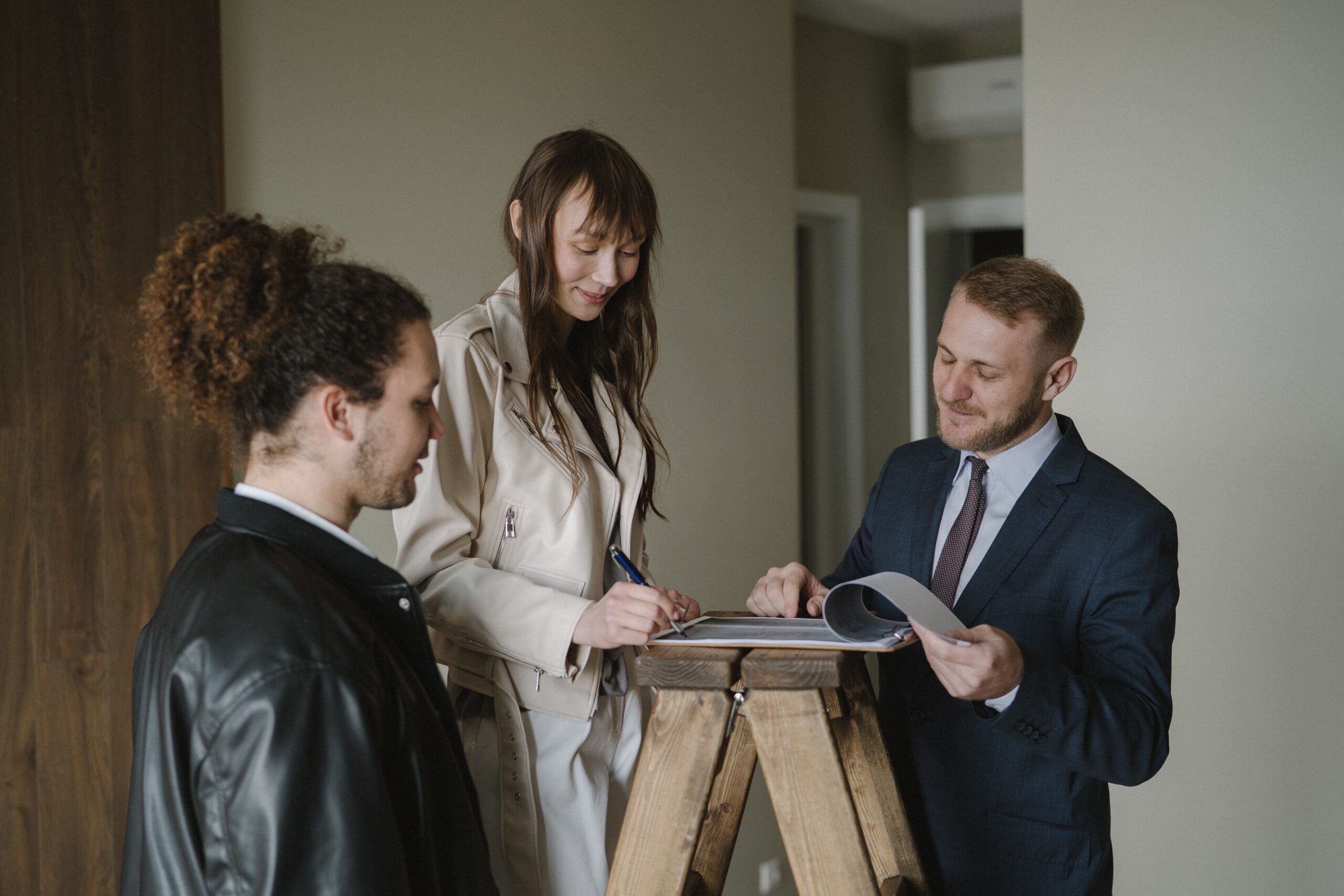 A woman signing property documents while a suited man looks on inside an apartment.